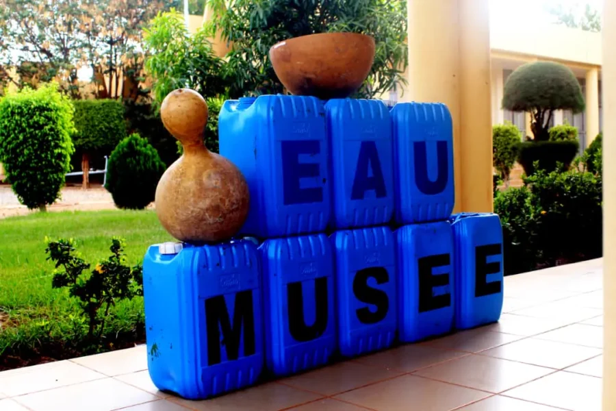 Bidons bleus peints « EAU MUSÉE » surmontés de calebasses.